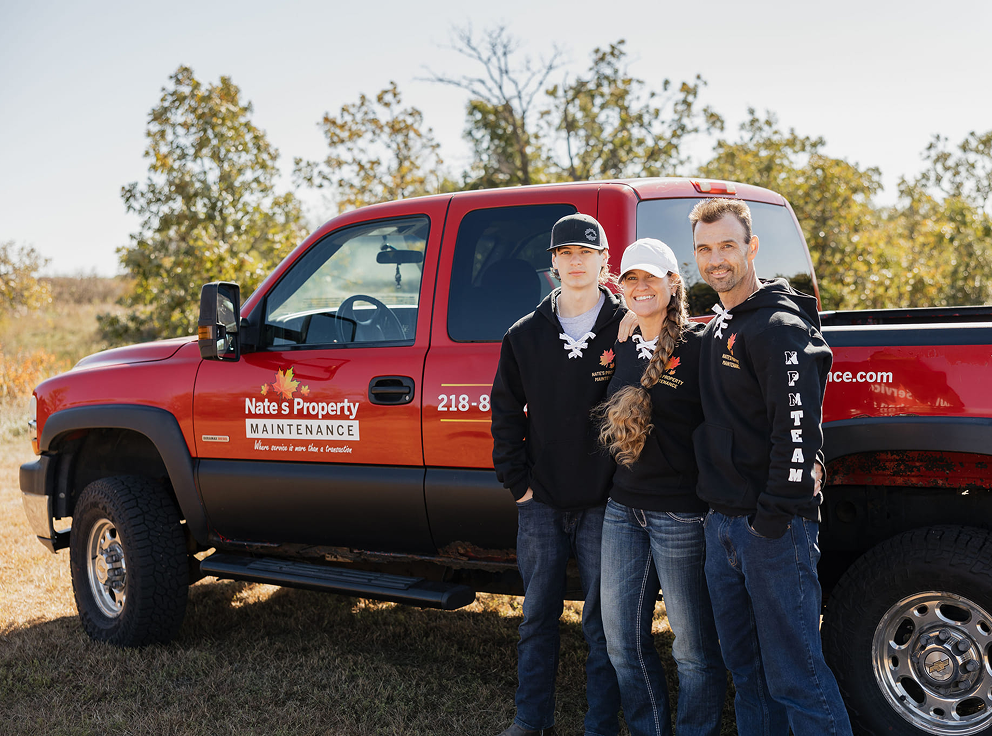 Three people posing in front of a red Sherwin-Williams truck outdoors.