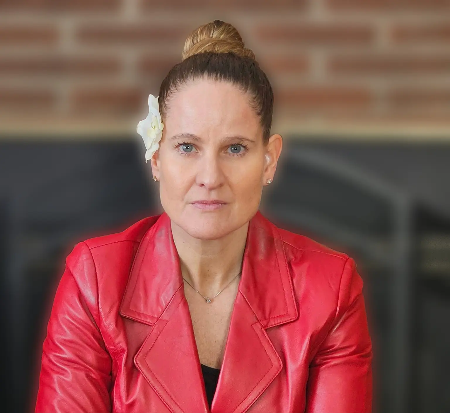 Woman in red jacket posing indoors against a brick background.